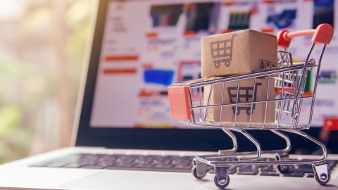 Laptop with online shopping screen and miniature shopping cart with tiny boxes