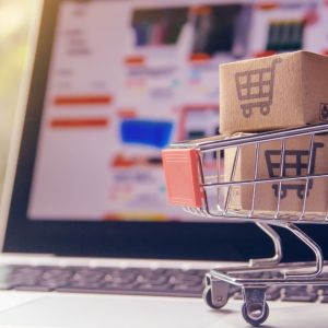 Laptop with online shopping screen and miniature shopping cart with tiny boxes